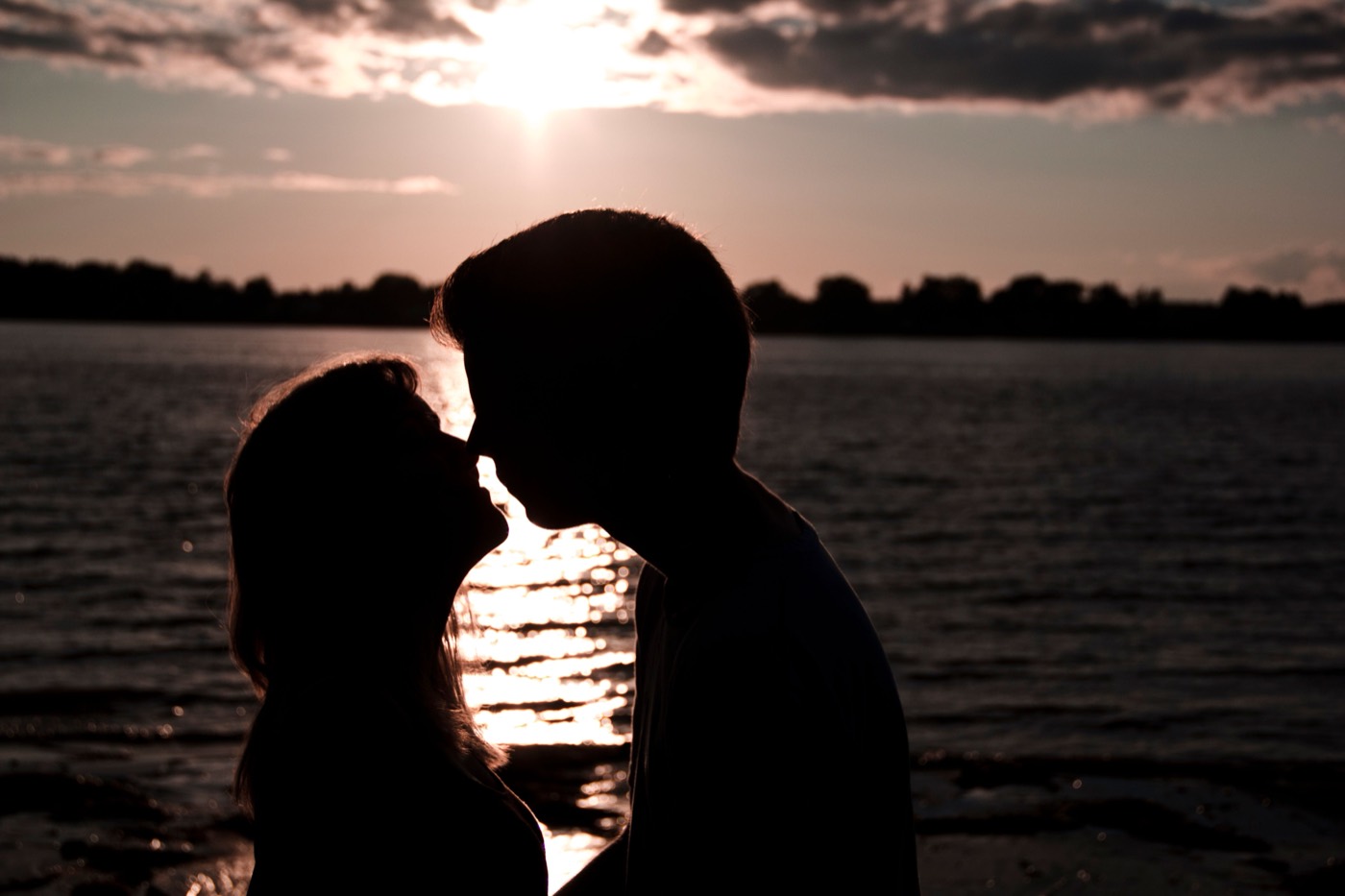 A couple stands in silhouette on a shore at sunset